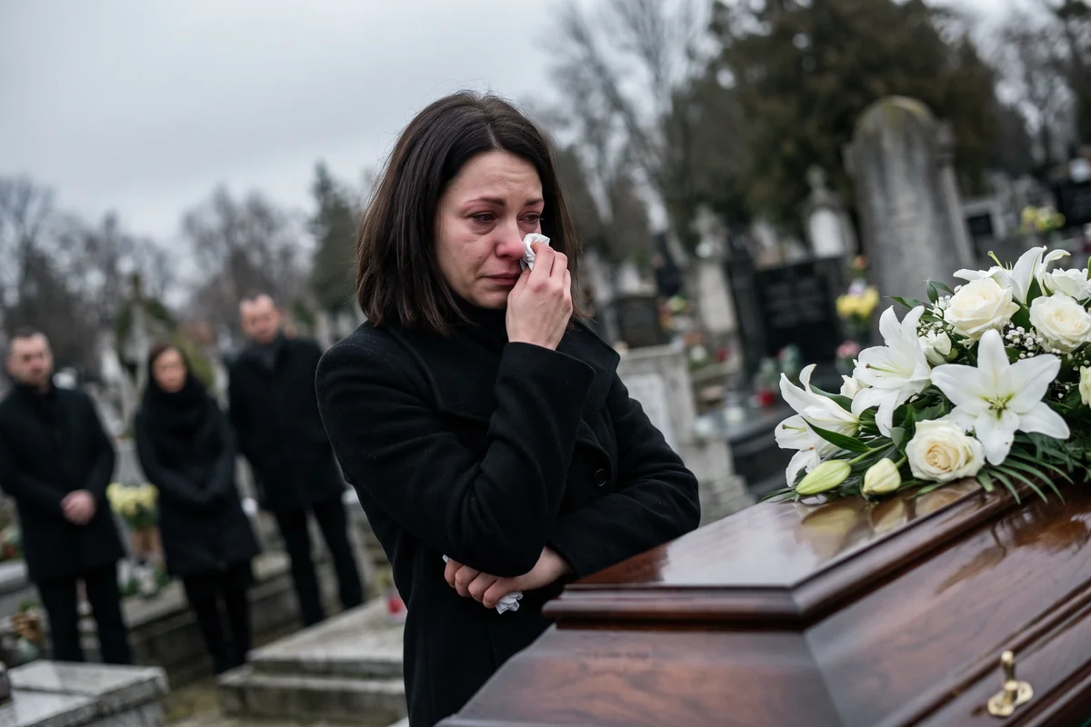 A woman in black crying beside a casket at a cemetery